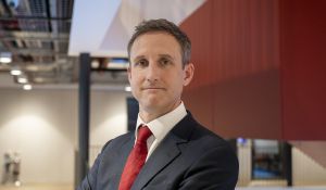 A headshot of Sam Lister in a suit